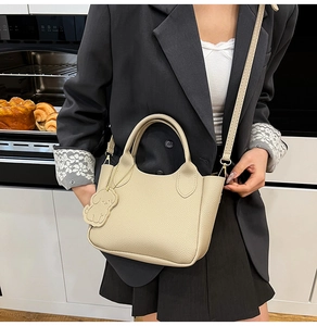Détail du sac seau en cuir blanc cassé avec breloque chien dans un décor moderne