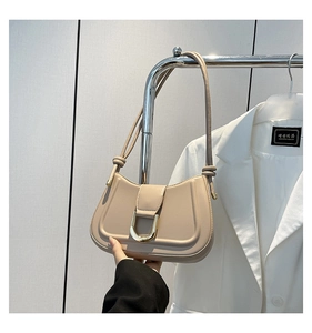 Detail of beige saddle bag featuring gold D-buckle hardware and smooth leather finish