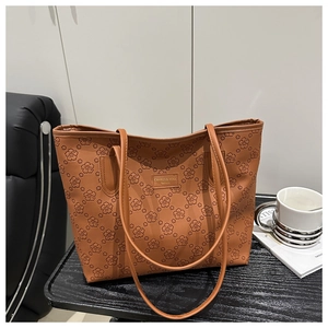 Close-up of brown leather tote bag with embossed floral texture on a dark wooden table