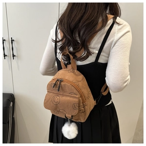 Brown corduroy mini backpack with smiley face pattern and white plush ball charm