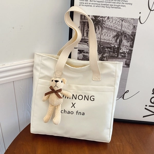 Off-white large canvas tote bag with letter print and cute teddy bear pendant on wood desk