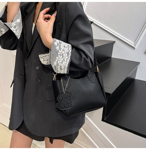 Détail du sac seau noir en cuir grainé avec finitions dorées et breloque chien sur modèle