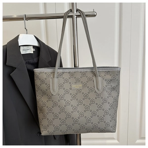 Detail of grey tote bag featuring floral prints and a golden metallic logo plate