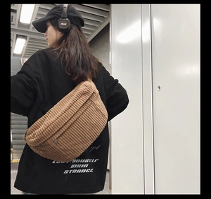 Side view of a brown corduroy crossbody bag worn by a model in a modern indoor setting