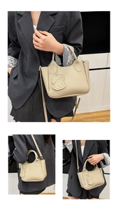 Détail du sac seau en cuir beige avec charme de chiot et bandoulière amovible