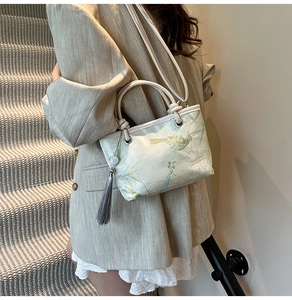 Detailed embroidery of birds and bamboo on a light green bucket bag with a gray tassel