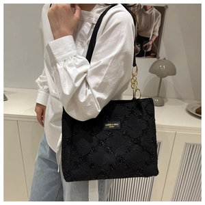 Detail view of black quilted nylon tote bag with golden chain and branded fashion plate