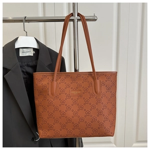 Close-up of brown floral embossed tote bag featuring a metallic logo plate detail