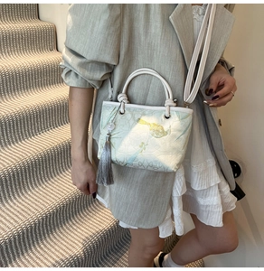 Detail of green embroidered bucket bag with magpie pattern and silk tassel on model