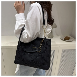 Detail of black quilted nylon tote bag featuring gold ring accents and chain strap