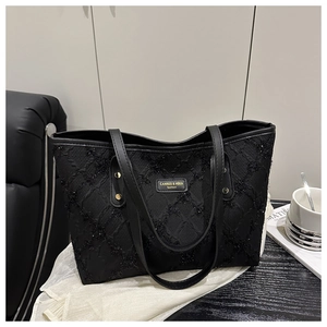 Detail of black tote bag with quilted sequin texture and metallic brand plaque