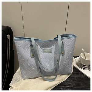 Close-up of light blue quilted tote bag featuring delicate floral embroidery and metal tag