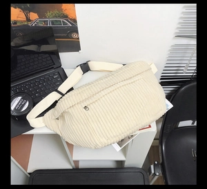 Detail of off-white corduroy chest bag showing fabric texture and metal zipper pocket