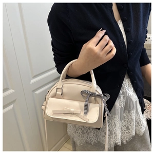 Detail of a beige leather handbag featuring a plaid ribbon bow and front pocket accessory