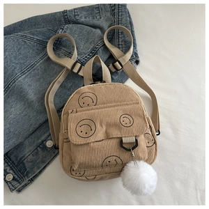 Detail view of beige corduroy backpack with smiley prints and fluffy white ball pendant