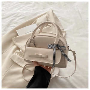 Detail of beige shell bag featuring a bow decoration and black-white checkered ribbon
