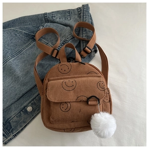 Detail of a brown corduroy mini backpack with a black smiley face and a white pompom charm