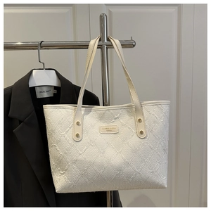 Detail of white quilted tote bag featuring textured fabric and metal logo plate