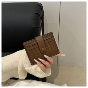 Close-up of brown woven leather card holder with buckle closure held in hand