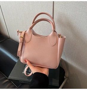 Détail de la texture cuir rose grainé et des boucles dorées sur le sac seau
