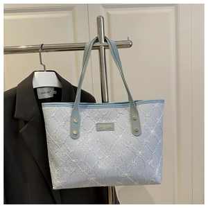 Close-up of light blue quilted floral tote with golden rivets and metallic brand logo