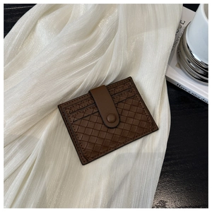 Detail view of deep brown woven leather card holder with snap closure on white fabric