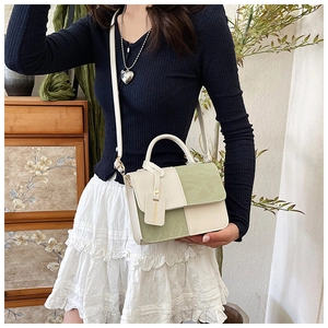 Detail of a white and green color-block handbag with a fashion decorative hangtag