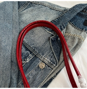 Detail of denim texture and red patent leather handle with vintage metal button