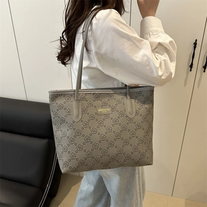 Gray floral tote bag with gold logo plaque, worn over the shoulder by a female model