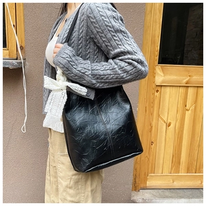 Detail of black pleated faux leather bucket bag with a white lace bow on the side
