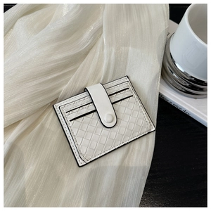 Close-up of a white woven card holder with button closure on soft silk fabric