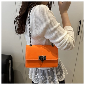 Rückansicht eines Modells mit orangefarbener Lackleder-Umhängetasche und Metallkette