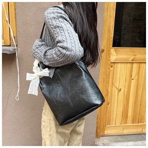 Close-up of black tote bag featuring delicate white lace bow and textured pleats