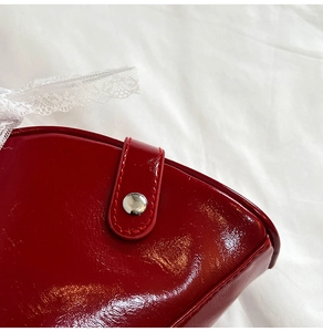 Detail of red patent leather shoulder bag with silver snap button and white lace trim