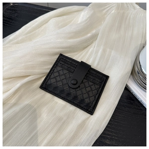 Close-up of black woven leather wallet with snap closure on a soft white fabric background