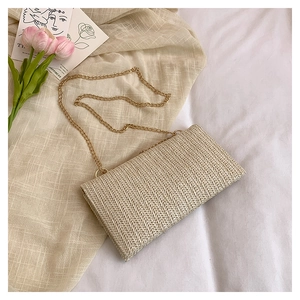 Detail of woven straw envelope bag with gold chain strap on beige linen fabric