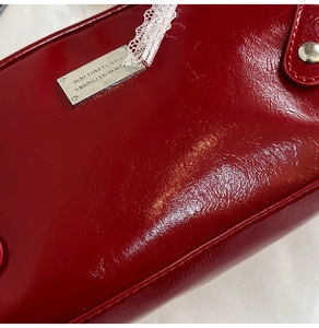 Detail of red patent leather shoulder bag with silver metal tag and lace accents