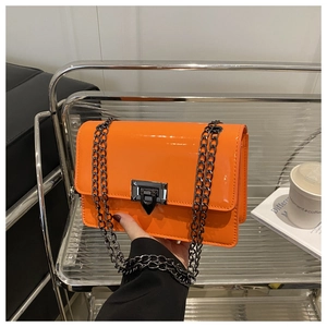 Detail of bright orange patent leather square bag with dark metal chain and twist lock
