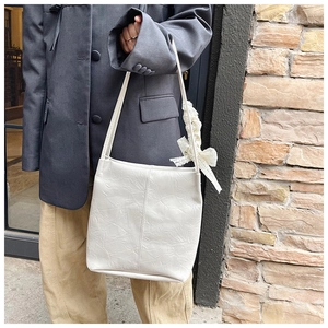 Detail of ivory pleated tote bag with a lace bow pendant on a shoulder strap