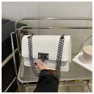 Detail of white patent leather crossbody bag featuring a metallic chain and turn-lock closure