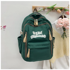 Dettaglio dello zaino in nylon verde scuro con stampa di lettere bianche e cerniere