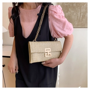 Detail of hand-woven straw shoulder bag featuring gold chain strap and metal lock closure
