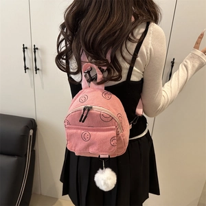 Pink corduroy mini backpack with black smiley face prints and a white fuzzy keychain