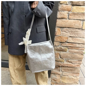 Close-up of metallic silver tote bag with pleated texture and white lace bow detail