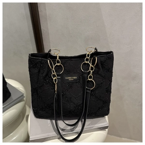 Detail of black tote bag with gold chain handle and brand logo on book background