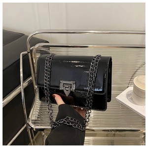 Detail of black glossy chain bag with gunmetal lock mechanism on a minimalist table