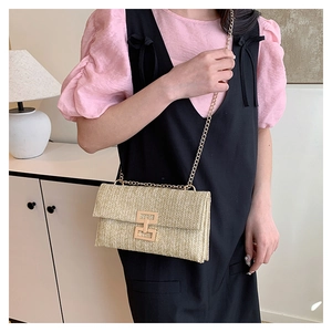 Close-up of woven straw crossbody bag featuring golden chain strap and geometric metal clasp