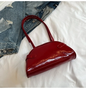Detail of burgundy patent leather underarm bag with glossy finish on white bedding