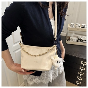 Detail of cream half-moon crossbody bag with gold chain and plush lamb charm