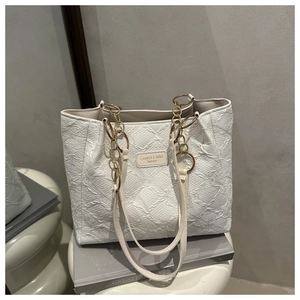Detail of white quilted tote bag with golden chain straps and textured faux leather finish